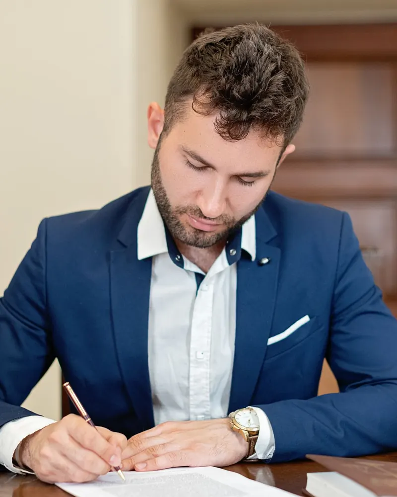 A man in a suit signing a document at a desk